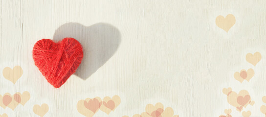 Red heart made of wool threads on a light wooden background