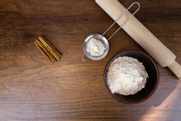 Flour in a wooden bowl, a small sieve and cinnamon sticks on a wooden table. Side view with copy space. Kitchen baking tools with place for text, or logo.