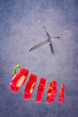 Ein in Scheiben geschnittener roter Paprika mit einer Schere vor einem blauen Hintergrund