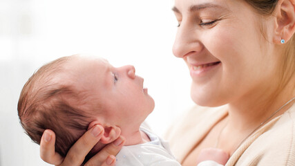 Closeup portrait of smiling mother with adorable newborn baby against big bright window. Concept of family happiness and loving parents with little children