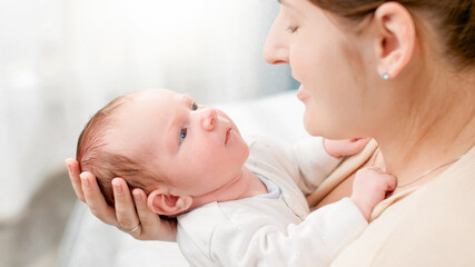 Above view on young caring mother hugging and cuddlingher newborn baby son in bedroom with big window. Concept of family happiness and loving parents with little children