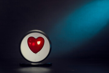 A red heart-shaped balloon is reflected in a round mirror on a dark background.