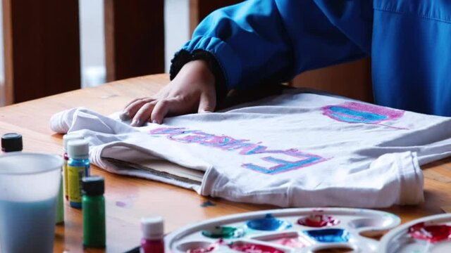 The child's hand makes a drawing on the shirt. Hand holds brush, applies paint to the fabric. Children creativity in isolation. DIY clothes.