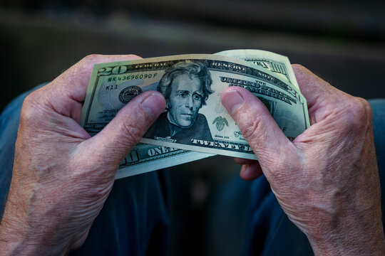 Elderly man holding US dollar bills in hands, 20 dollar note in pensioner's hand
