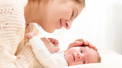 Closeup portrait of loving young mother stroking her 1 months old baby boy lying on bed. Concept of family happiness and loving parents with little children
