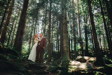 Happy stylish couple newlyweds in the green forest on summer day. bride in long white dress and...