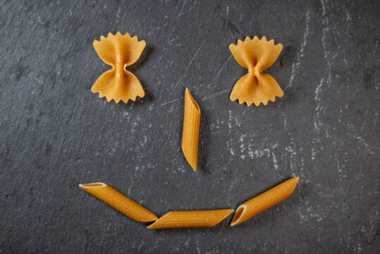 Wholemeal pasta. Pasta used to compose a smiley face on a slate dish. Healthy nutrition concept