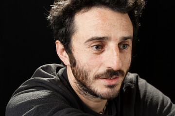 Handsome adult white man with beard and green eyes on a black background and casual expression. 