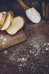 Flour in a wooden spoon, sliced French baguette on a wooden board, and cinnamon sticks sprinkled with flour on a wooden table. side view
 with place for text or logo. Retro photo.