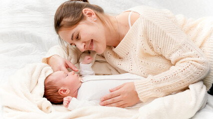 Happy smiling mother playing and tickling her 1 months old newborn baby lying on bed. Concept of family happiness and loving parents with little children