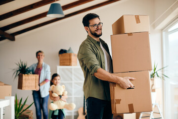 Happy man carrying stack of carton boxes while moving with his family into new home. - Powered by Adobe