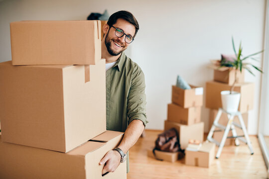 Happy man carrying stack of cardboard boxes while relocating in a new apartment.