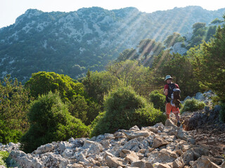 Man hiker at rocky hiking path to Cala Goloritze beach with limestone rocks, trees and green bush....