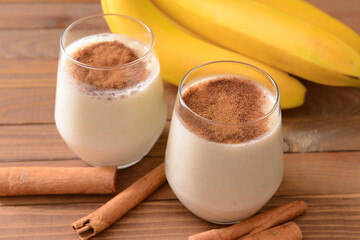 Tasty banana smoothie with cinnamon in glasses on wooden background