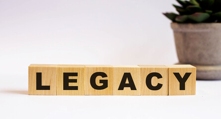 The word LEGACY on wooden cubes on a light background near a flower in a pot. Defocus