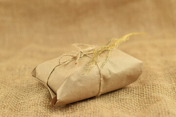 Simple eco friendly gift box package wrap with brown paper. Burlap background. Delivery of ecological products, eco-friendly packaging, craft. Green present concept, copy space.