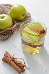Tasty apple drink with cinnamon in glass on light background