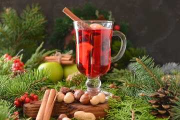 Tasty mulled wine with cinnamon in glass on Christmas tree branches