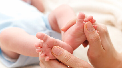 Closeup of young caring and loving mother massaging and stroking little feet of her newborn baby son lying in bed. Concept of family happiness and loving parents with little children. Baby massage and