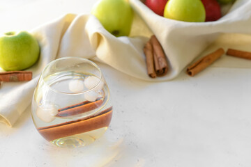 Tasty apple drink with cinnamon in glass on light background