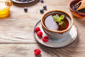 Cup of hot tea with mint and berries on wooden background