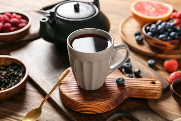 Board with cup of hot fruit tea on wooden background