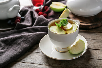 Cup of hot tea with apples and mint on wooden background