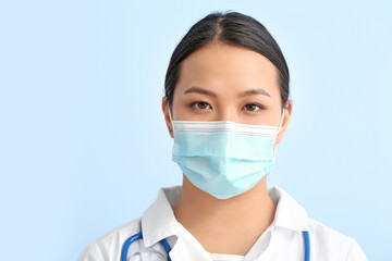 Portrait of female Asian doctor in medical mask on color background