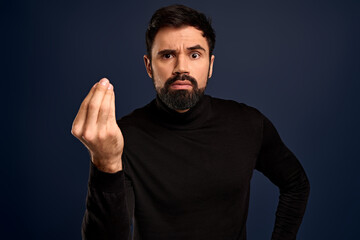 Fototapeta premium Where is my money. Serious-looking confident young bearded businessman in high neck sweater, showing cash gesture, rubbing fingers against each other and smirk displeased, someone own him