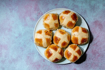 Homemade Easter traditional hot cross buns on ceramic plate over blue texture background. Flat lay, space