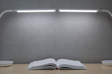 An open book lies on a wooden table. On both sides of the book are two table lamps.