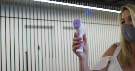 Caucasian businesswoman wearing face mask checking coworkers temperature - Powered by Adobe