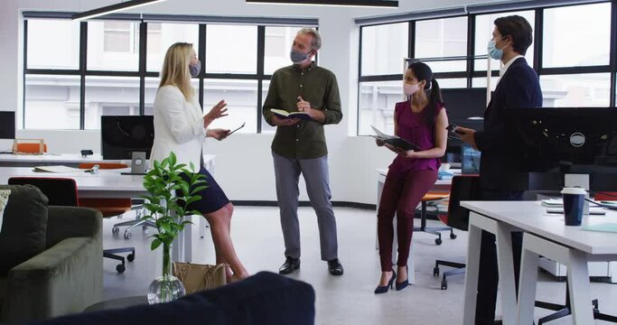 Diverse business colleagues wearing face masks having casual meeting standing in office