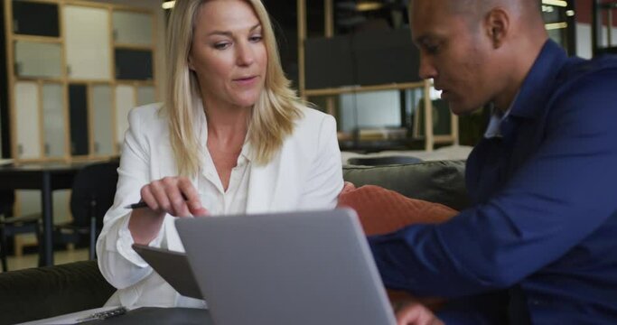 Two diverse business colleagues using laptop and discussing in a casual meeting