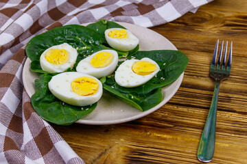 Boiled eggs with fresh spinach leaves and sesame seeds on wooden table