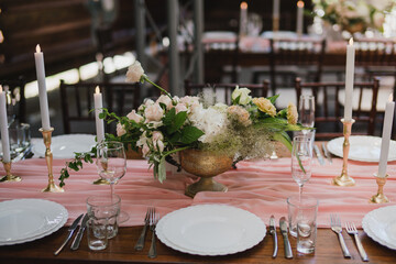 Coziness and style. Modern event design. Table setting at wedding reception. Floral compositions with beautiful flowers and greenery, candles, laying and plates on decorated table.