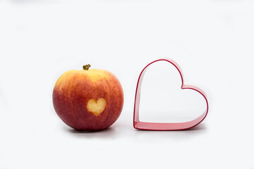 Red Juicy apple with a heart shape cut-out and heart shaped cookie cutter. Isolated on white background