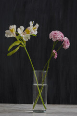 Flores de colores en un vaso de cristal con un fondo oscuro sobre una base de mármol. Concepto decoración de interiores minimalista