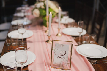 Coziness and style. Modern event design. Table setting at wedding reception. Floral compositions with beautiful flowers and greenery, candles, laying and plates on decorated table.