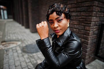 Fashionable beautiful african american woman posing in black leather jacket at street. Earring in the nose.