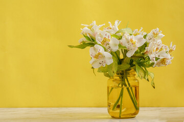 Florero amarillo con ramo de flores blancas sobre una mesa de mármol y fondo de color amarillo....