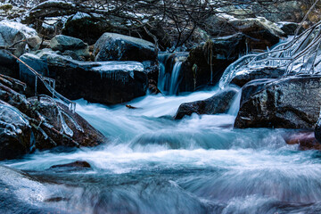 Mountain river frozen in winter with very cold blue water. The water flows down a mountain stream. Winter landscapes and background.