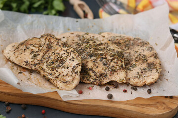 Chicken fillet with aromatic herbs on parchment on a wooden board. Closeup, healthy nutrition