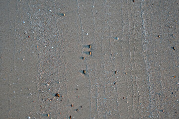 Sand on the beach with traces of receding water from the waves. Small pebbles.