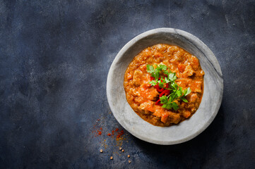 Chicken tikka masala spicy curry meat food in marble plate with spices and parsley on dark textured background with more empty space. Close up, top view. Indian food recipe.