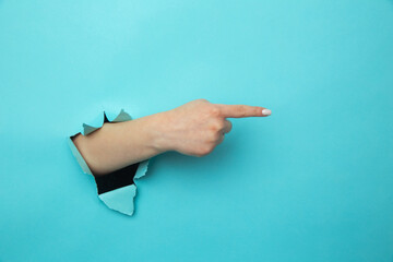 Woman breaks arm through paper blue wall indicates on right at blank space gives advice.