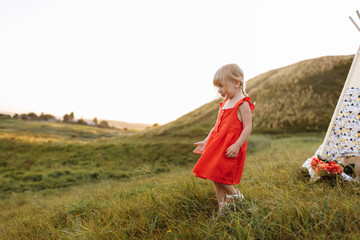 cute little girl is having fun near wigwam in a summer field on sunset. Young family spending time together on vacation, outdoors. The concept of summer holiday. © Andriy Medvediuk