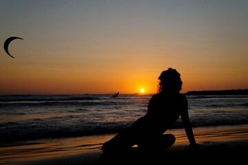 Silueta de mujer sentada a la orilla de la playa al atardecer