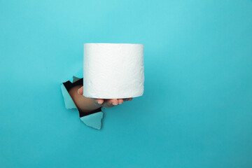 Female hand holds toilet paper through torn blue paper background.