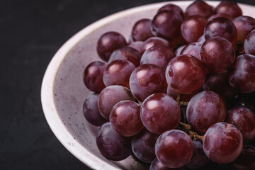 Fresh ripe grape berries in white wooden bowl on dark stone background, angle view macro